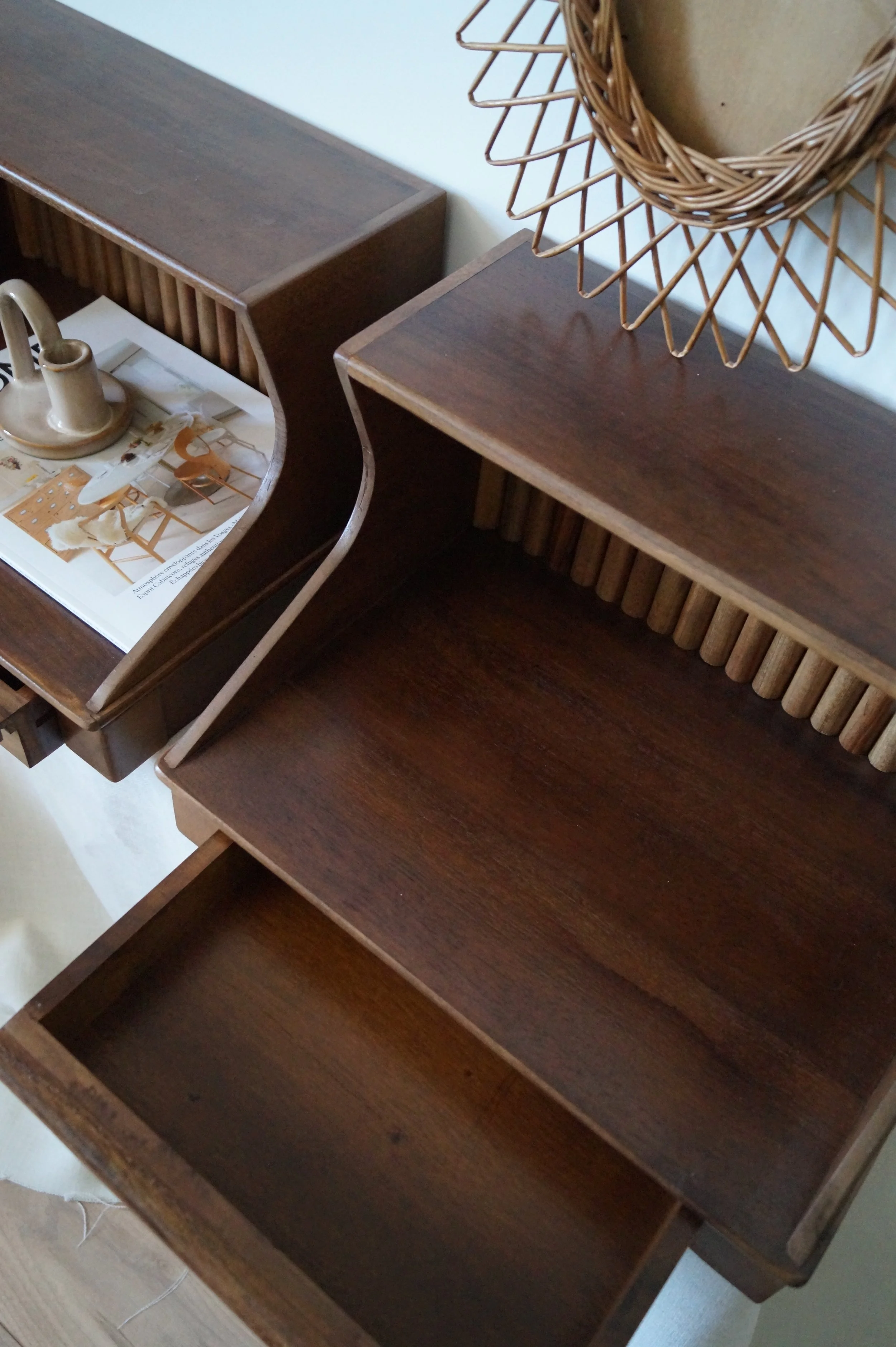 Deux meubles en bois avec des tiroirs ouverts. Sur le meuble de gauche, il y a un magazine et une petite décoration en céramique. Sur le meuble de droite, il y a un miroir avec un cadre en rotin.
