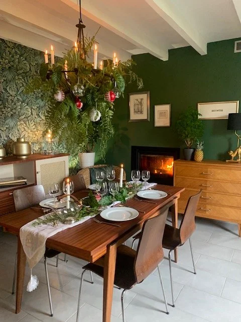 Salle à manger décorée pour Noël avec un sapin, chandelier, cheminée, et table prête à dîner.