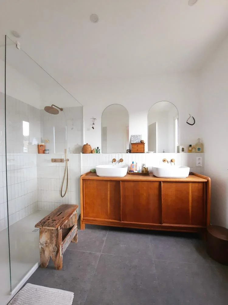 Salle de bain avec douche, double lavabo sur meuble en bois, miroirs arqués, décor en bois et accessoires