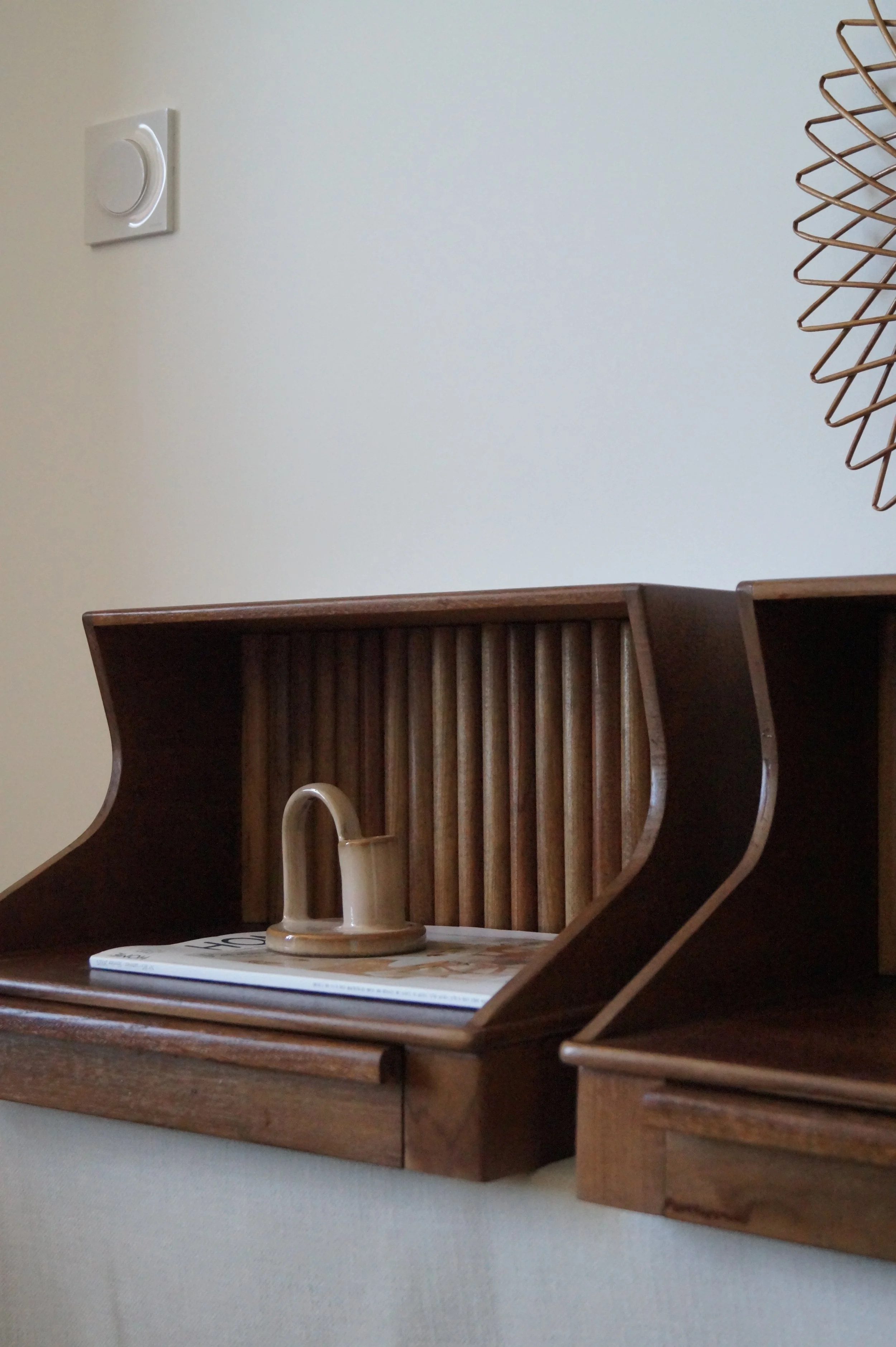 Une étagère en bois contenant un magazine et une petite casserole beige, avec un mur clair en arrière-plan.