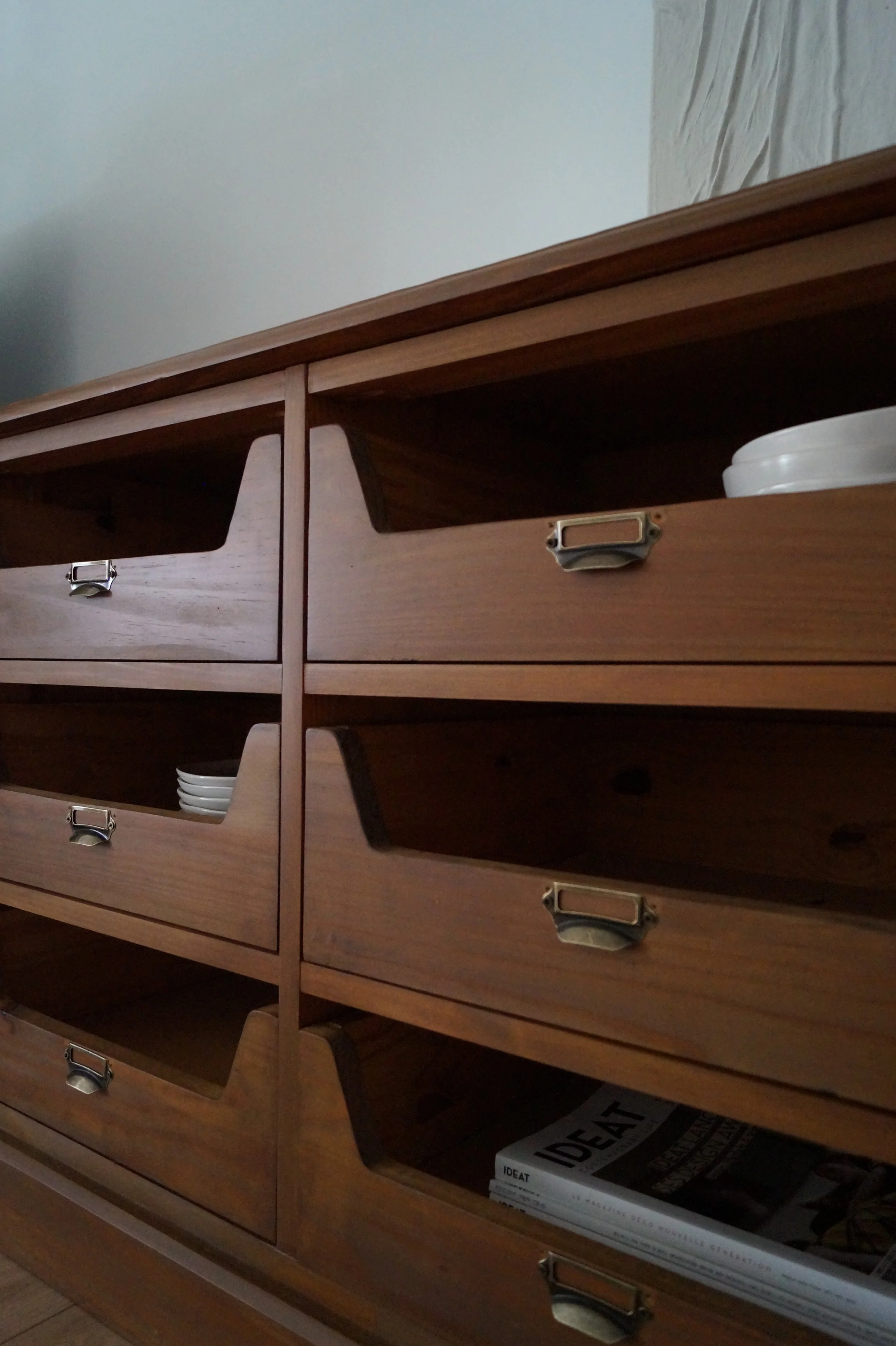 Un meuble en bois avec plusieurs tiroirs, certains tiroirs sont partiellement ouverts, contenant des assiettes et des magazines.