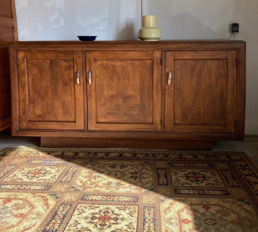 Un meuble en bois avec trois portes et poignée en métal, placé contre un mur blanc.