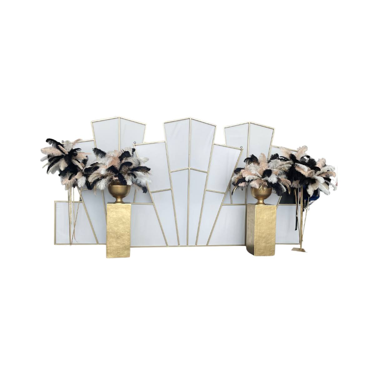 Decorative backdrop with geometric white panels, gold vases, and black and white feather arrangements.