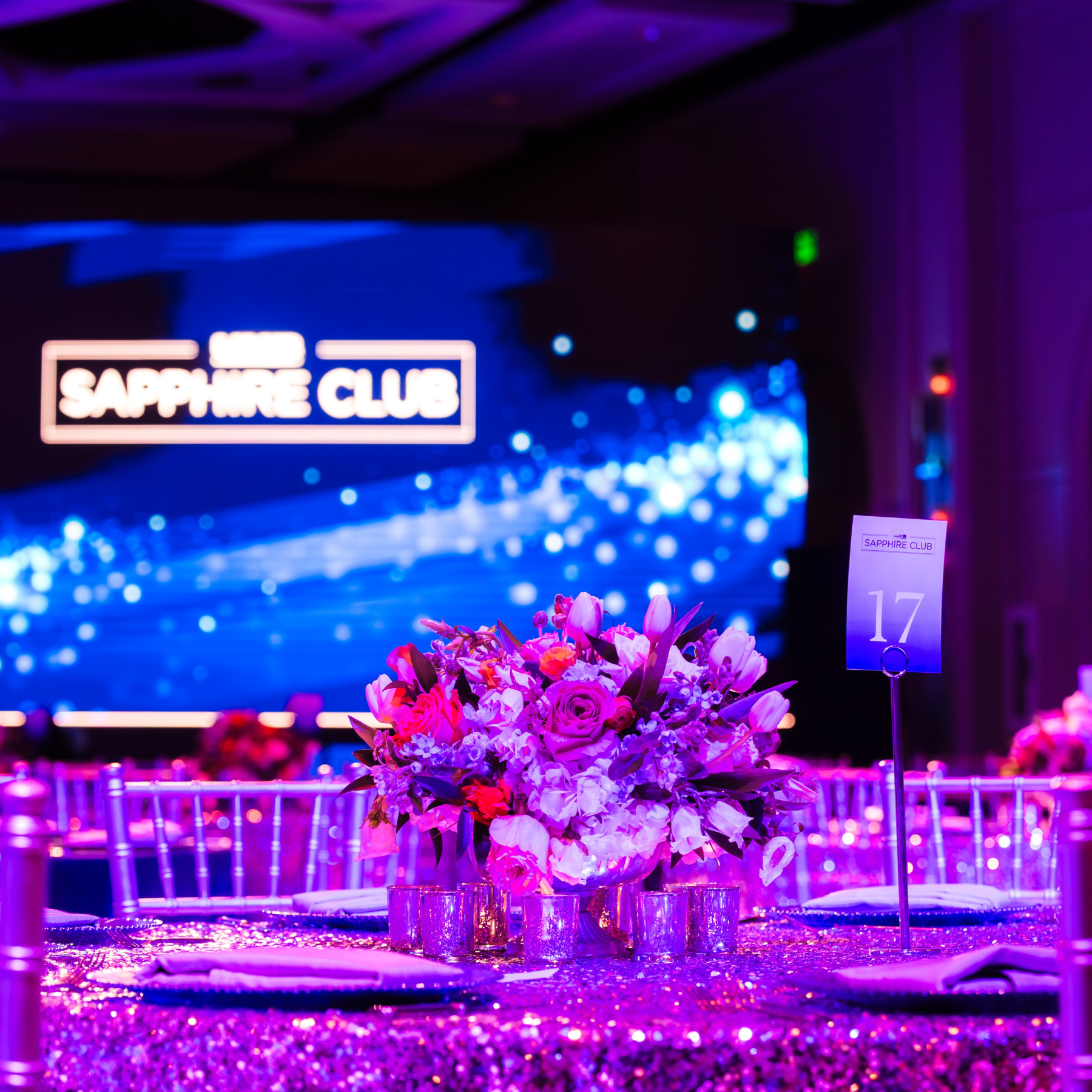 A modern house sits on green hills with snow-capped mountains in the background under a cloudy sky.