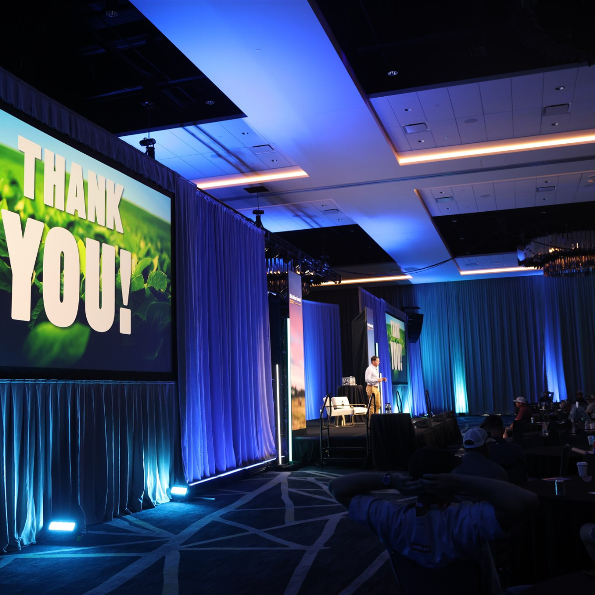 Modern house with large glass window, wooden exterior, situated in a mountainous landscape with dry grass and small trees.