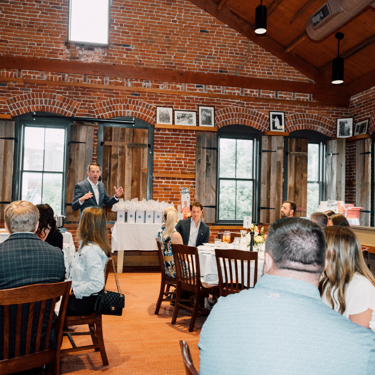 Modern house with large glass window, wooden exterior, situated in a mountainous landscape with dry grass and small trees.