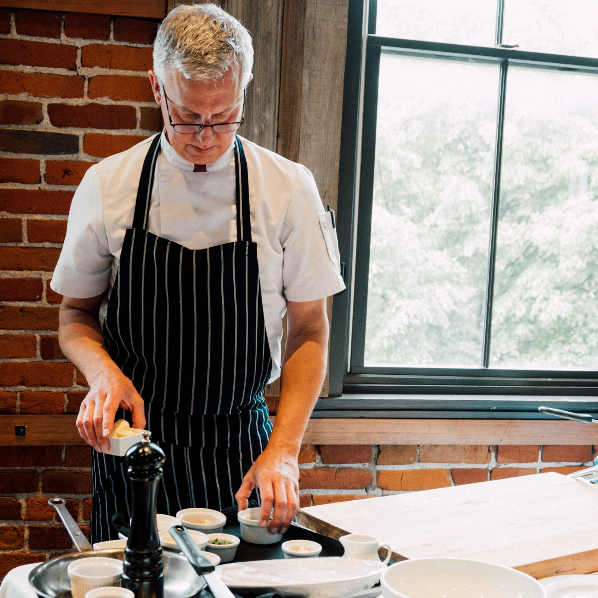 A modern house sits on green hills with snow-capped mountains in the background under a cloudy sky.