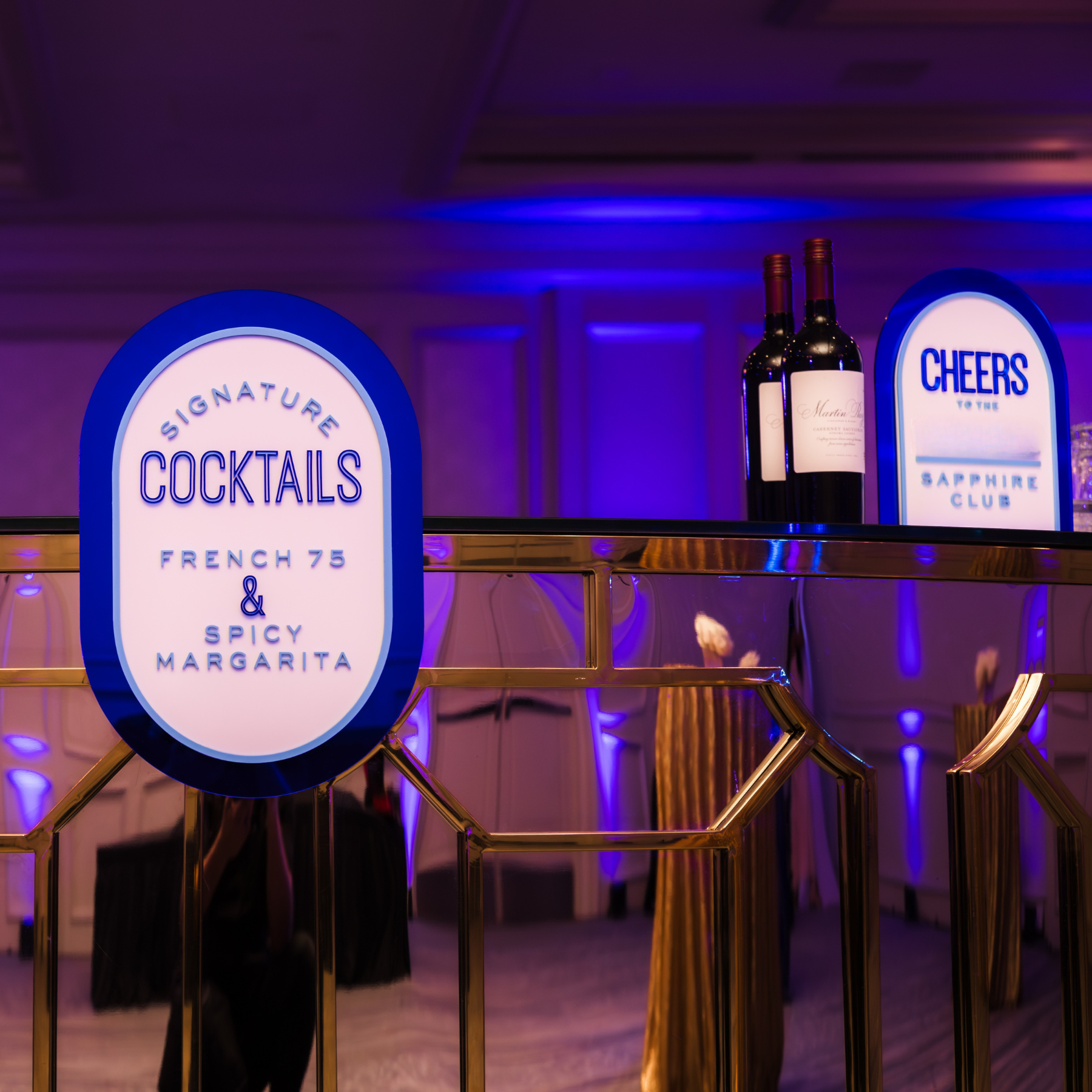 Modern wooden house with a flat roof, set in a grassy field with a few small trees, overlooking a large lake and distant mountains under a pinkish sky.