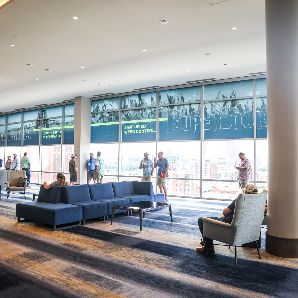 Modern wooden house with a flat roof, set in a grassy field with a few small trees, overlooking a large lake and distant mountains under a pinkish sky.