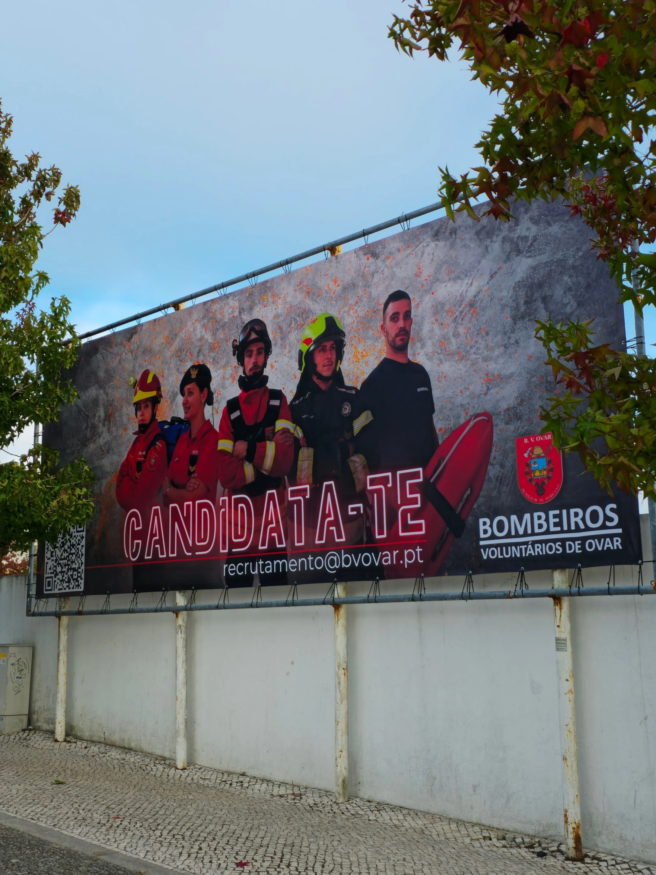 Painel de recrutamento para candidatos a bombeiros voluntários em Ovar, Portugal, com fotos de bombeiros vestidos com uniformes e equipamentos, e o logotipo do corpo de bombeiros.
