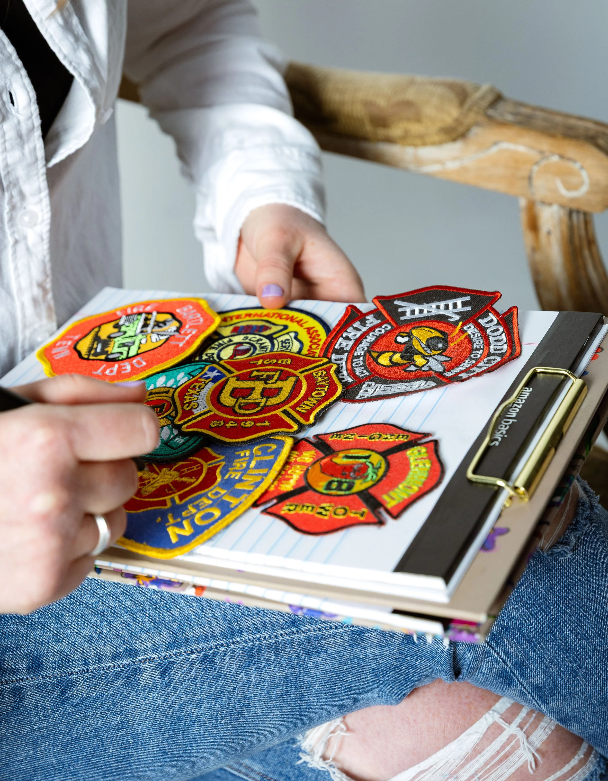 Close-up of hands writing on a notepad surrounded by first responder patches, symbolizing support for emergency personnel.
