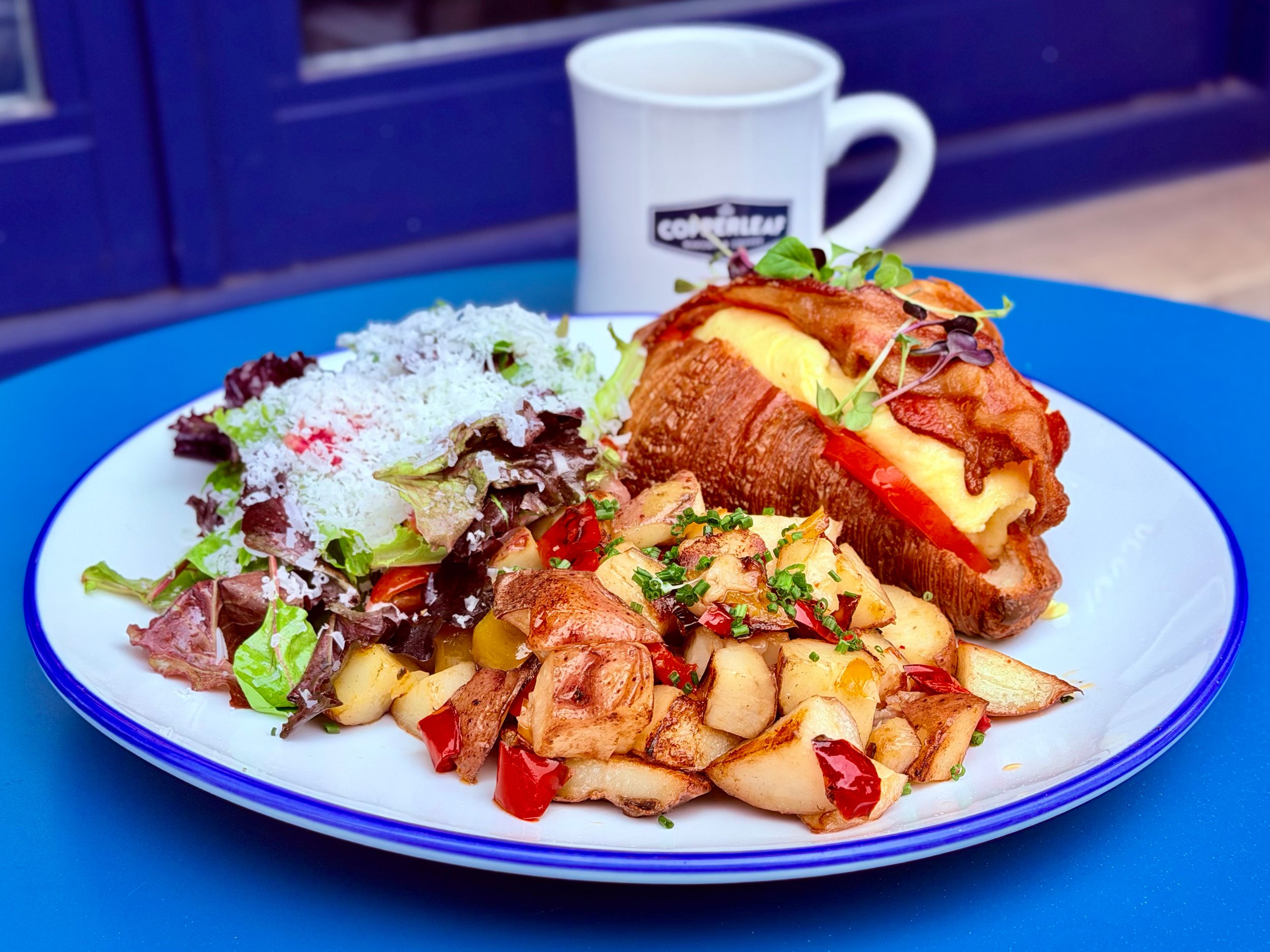 Freshly baked croissant breakfast sandwich with eggs and bacon, served with roasted potatoes and a side salad at CopperLeaf Bakery in Harlem.