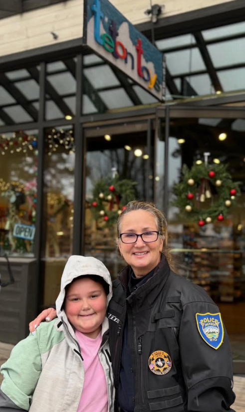 A woman in police uniform smiling with a young girl outside a colorful store called 'lemon' decorated for Christmas with wreaths and ornaments.