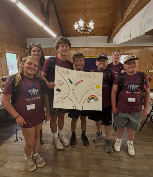 Group of six children holding a sign about anti-drug awareness in a wooden cabin or lodge.