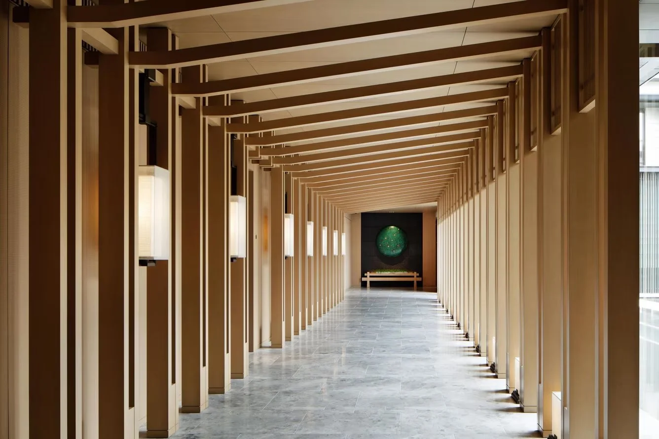 Modern architectural corridor with wooden slat walls, rectangular wall lights, gray tiled floor, and artwork at the far end.