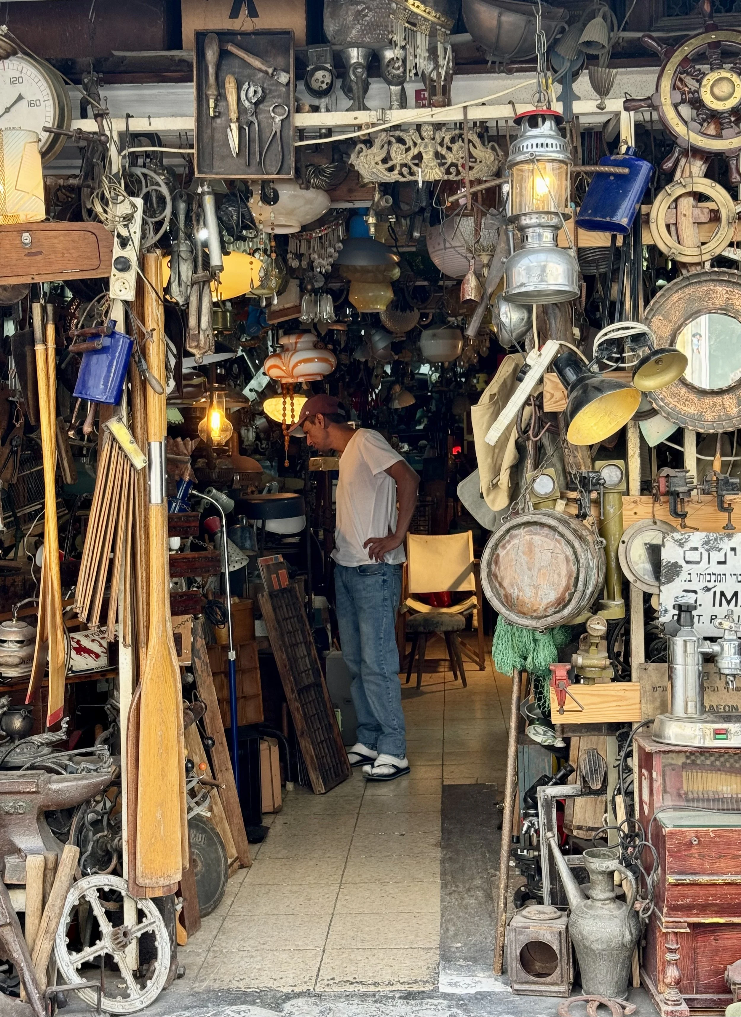 A man shopping in an antique store filled with vintage and retro items including lamps, tools, clocks, and various knickknacks.