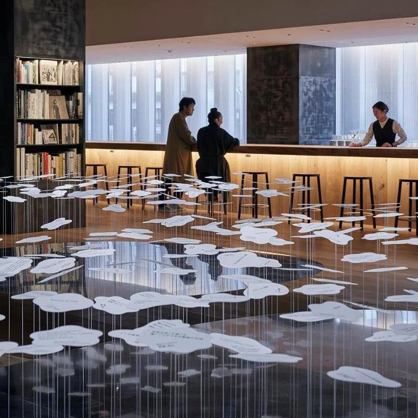 People at a bar counter in a modern interior with hanging paper art resembling clouds.
