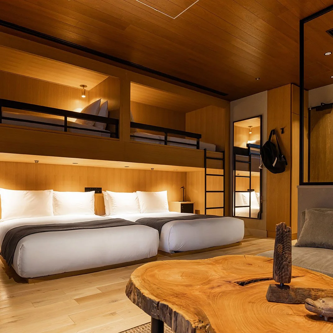 Hotel room with two large beds in the foreground and a loft bed above, wooden walls, and a rustic wooden coffee table.