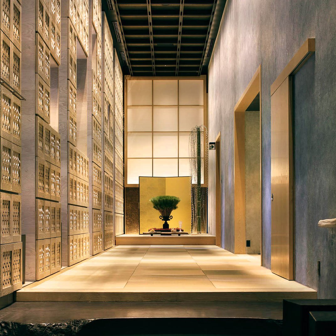 Modern hallway with wooden lattice walls, elevated platform, and a decorative plant in a black vase at the end.
