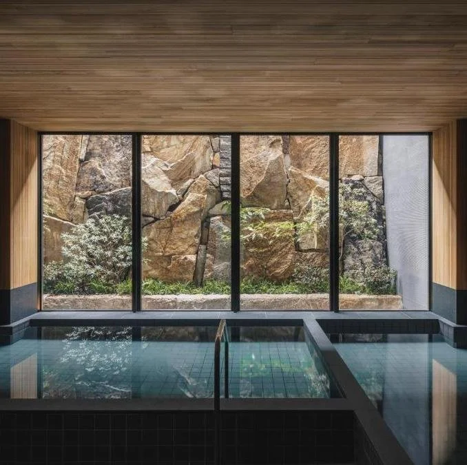 Indoor swimming pool with large glass windows showing rocky outdoor landscape.