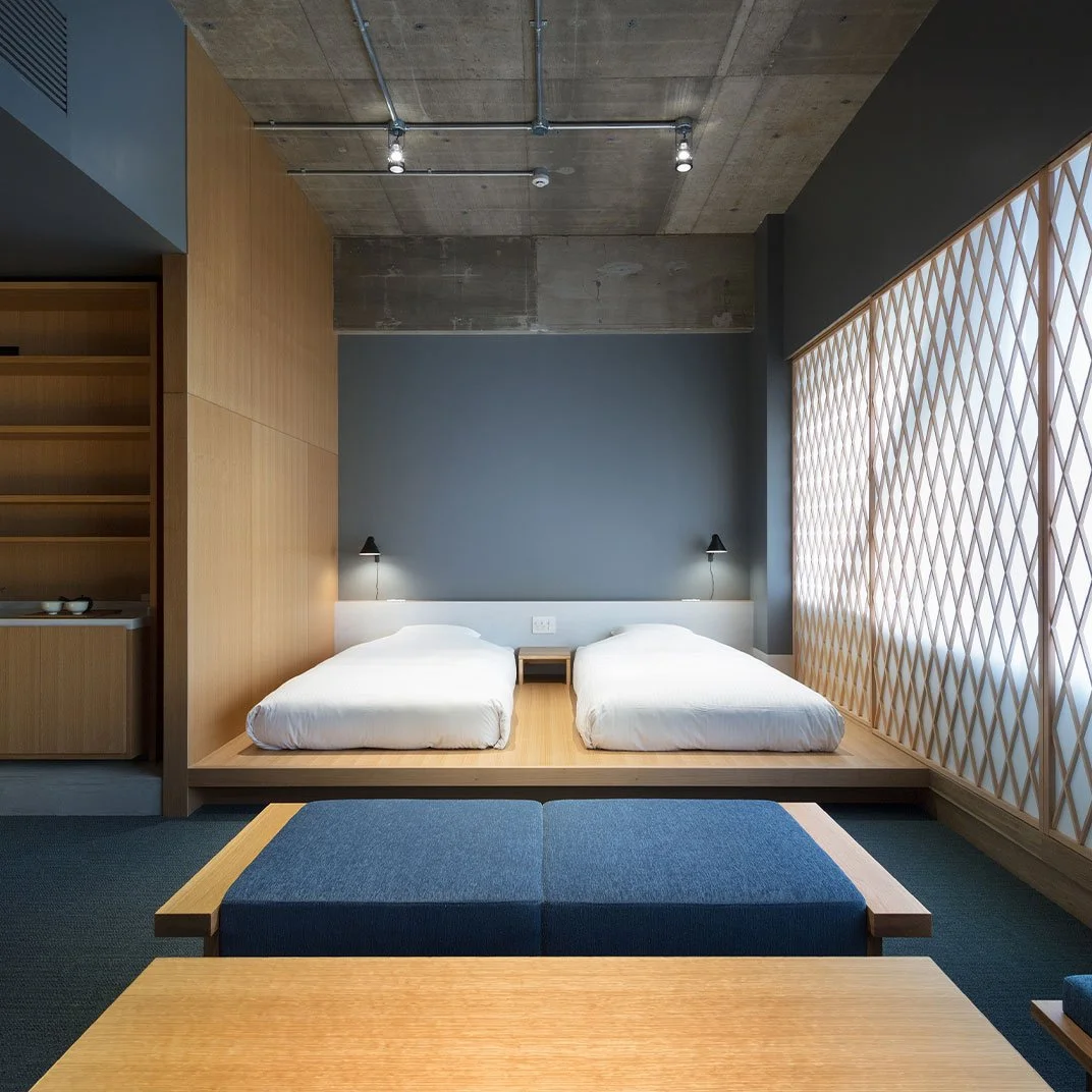 A modern hotel room with two beds, a blue wall, wooden accents, and a large window with a geometric patterned screen.