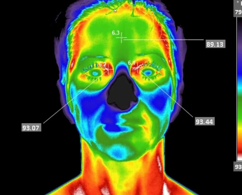 Thermal imaging of a woman's face showing various temperature levels with color coding. The image displays specific temperature measurements around the eyes, nose, and forehead.