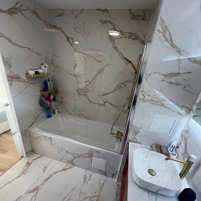 Bathroom with marble walls and floor, bathtub, and a small marble sink with a gold faucet.