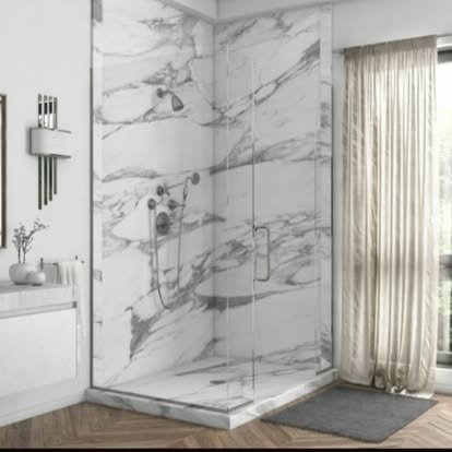 Modern bathroom shower with white marble walls, glass door, and curtain, with a gray rug on the wooden floor.