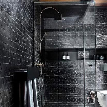Modern black-tiled bathroom shower with glass enclosure, built-in shelves, a showerhead, and towels hanging on a rack.