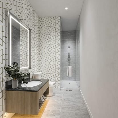 Modern bathroom with geometric patterned wall tiles, a backlit mirror, a black vanity with a white sink, and a walk-in shower with a glass door and a gray tiled wall.