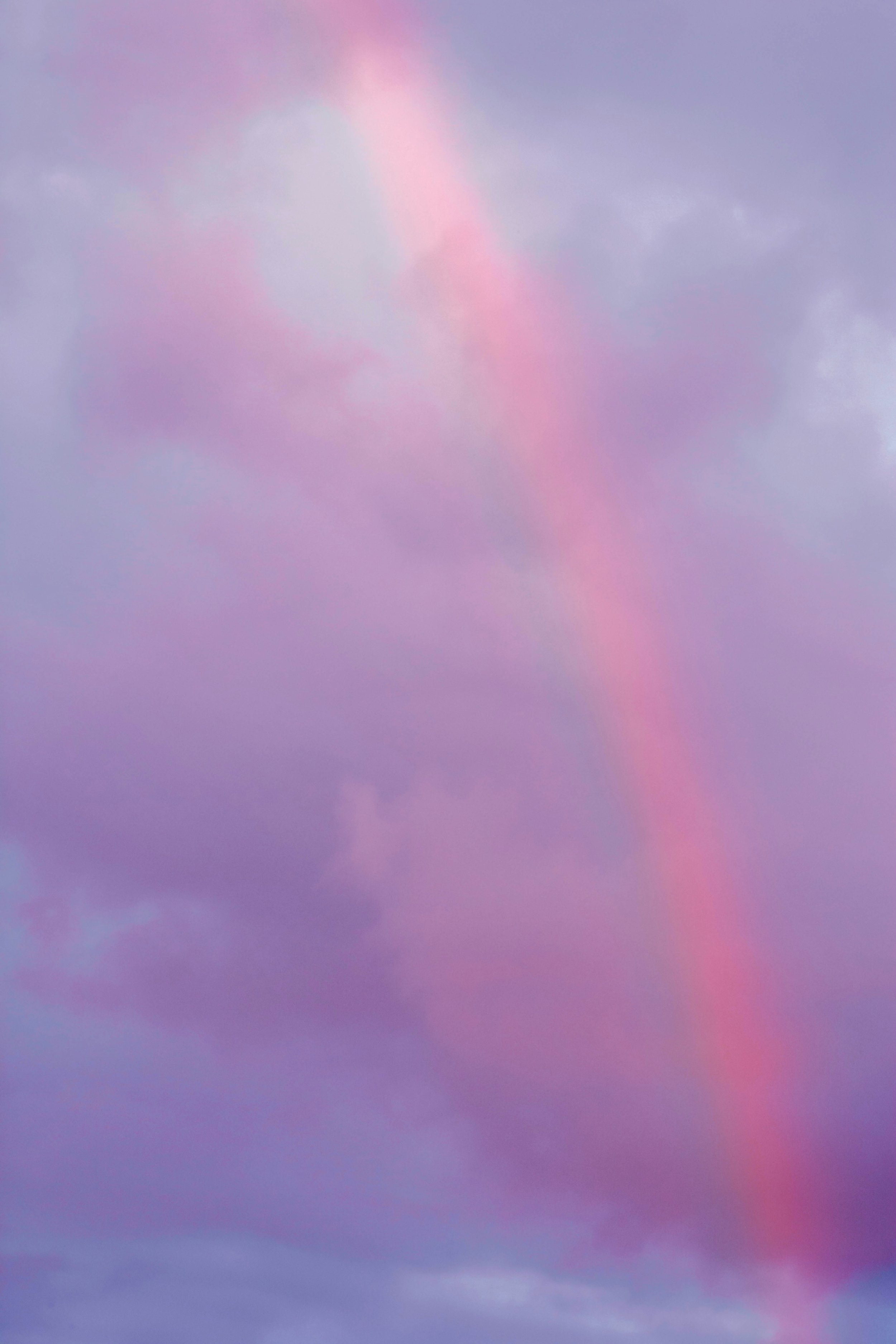 Pink and purple rainbow across cloudy sky.