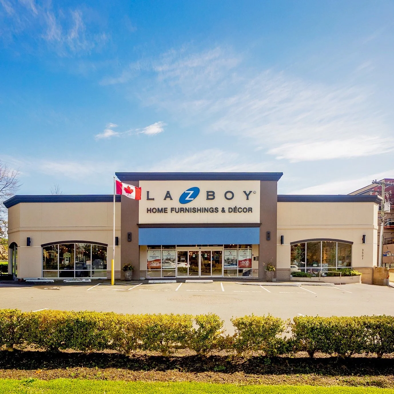 Exterior of a La-Z-Boy furniture store with a parking lot, shrubs in the foreground, and a clear blue sky. One of the best looking furniture stores on Vancouver Island