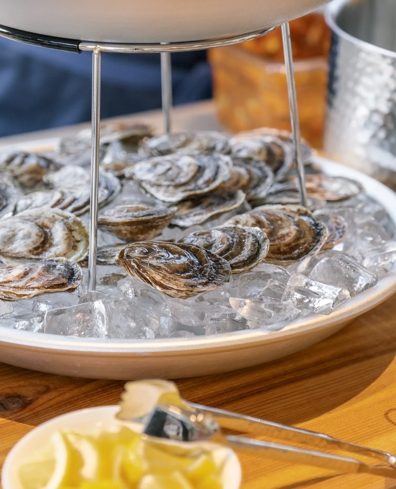A platter of fresh oysters on ice with lemon wedges nearby, at a seafood restaurant.