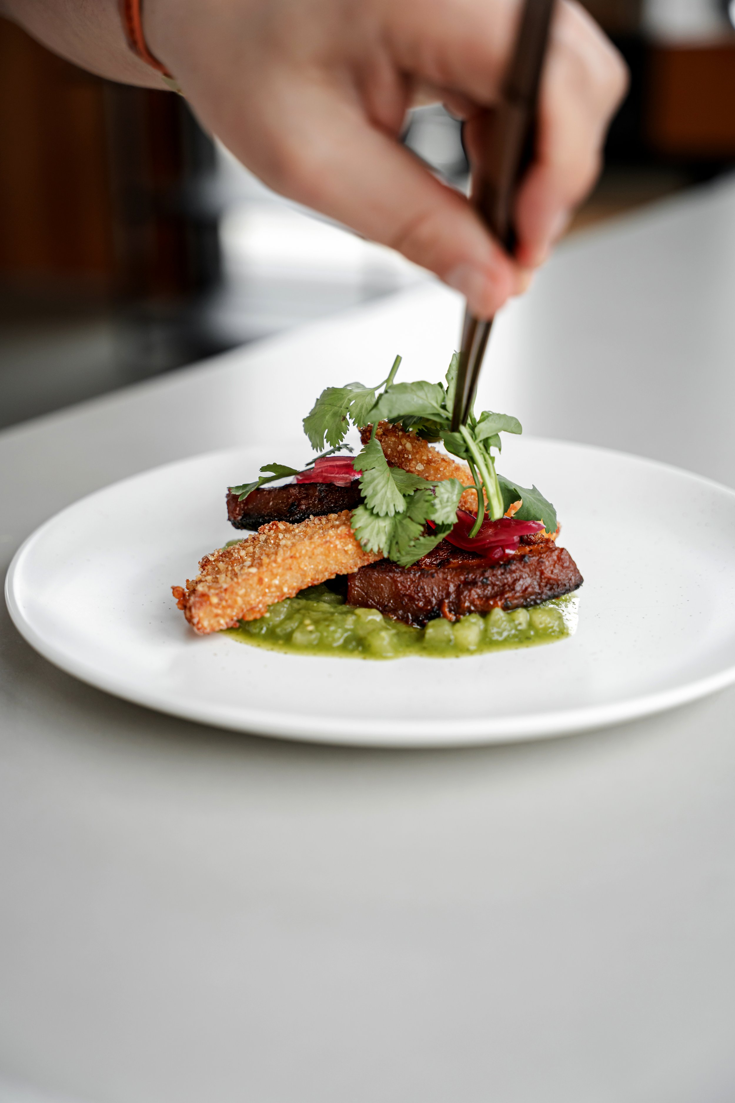 Person garnishing a gourmet dish with herbs using tweezers