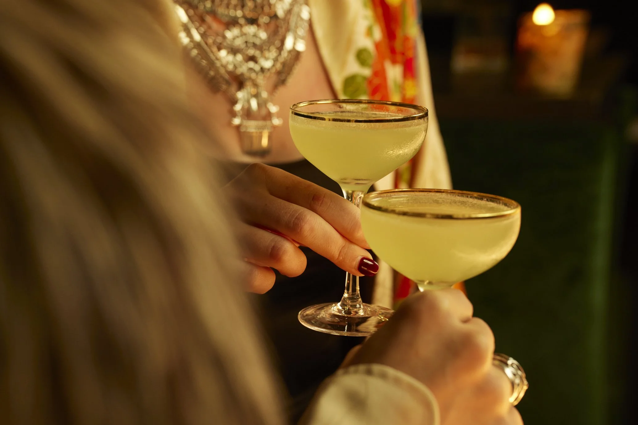 Two women holding cocktail glasses with light green drinks, celebrating at a social event.