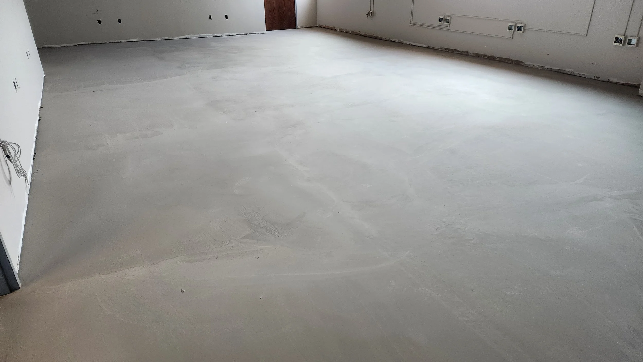 Bare concrete floor in an unfinished room with white painted walls, multiple electrical outlets, and visible wiring.