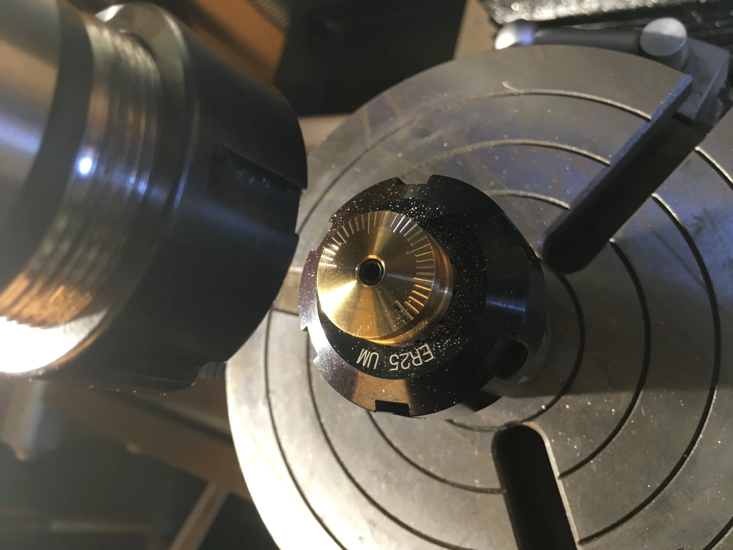 Ansicht der Spezialanfertigung eines Drehknopfes montiert in einem Spannzangenhalter auf einem Rundtisch. Zu sehen ist ebenfalls die Spindel der Fräsmaschine.