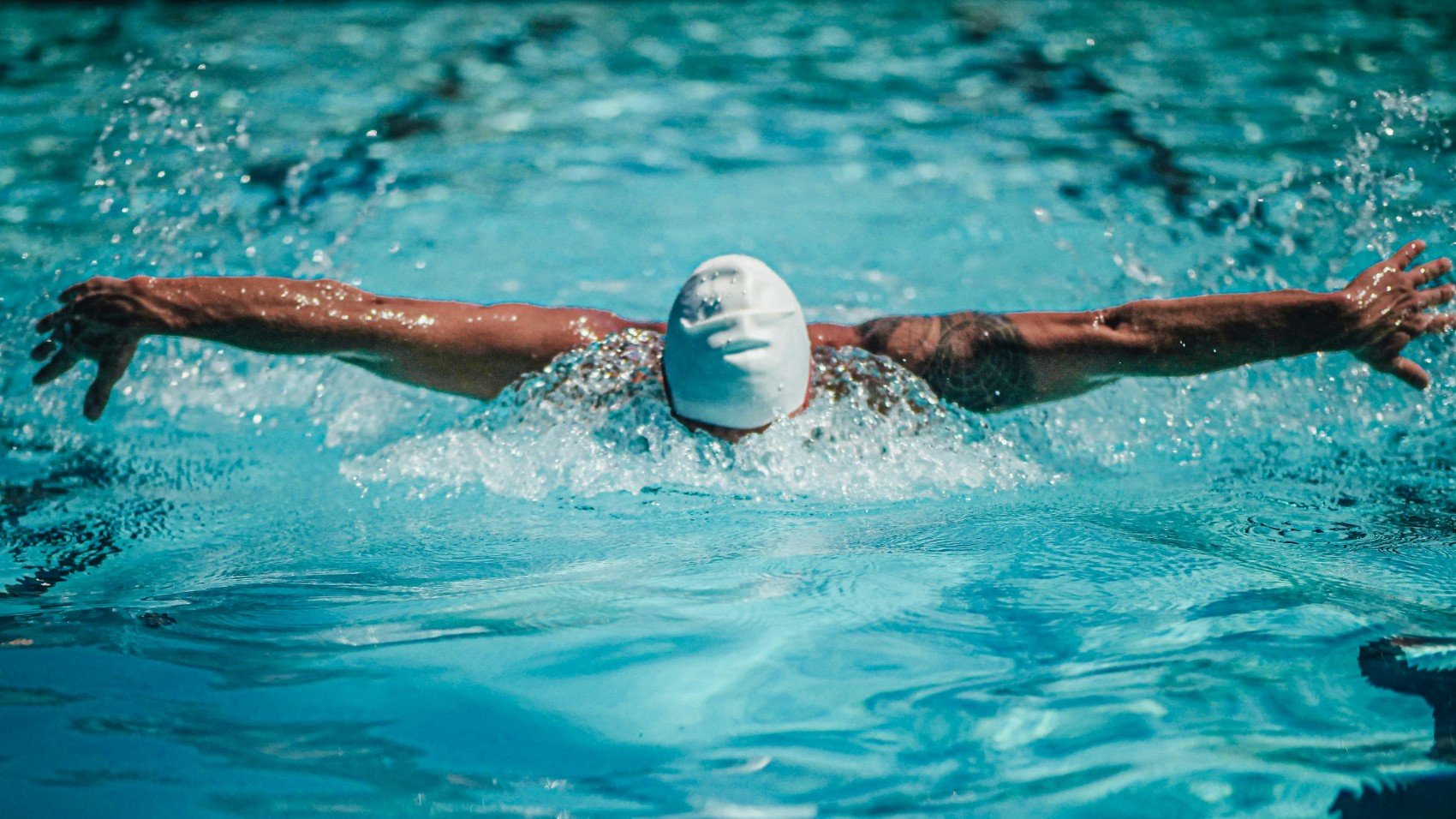 Swimmer in a pool wearing a white swim cap, executing a front crawl stroke.