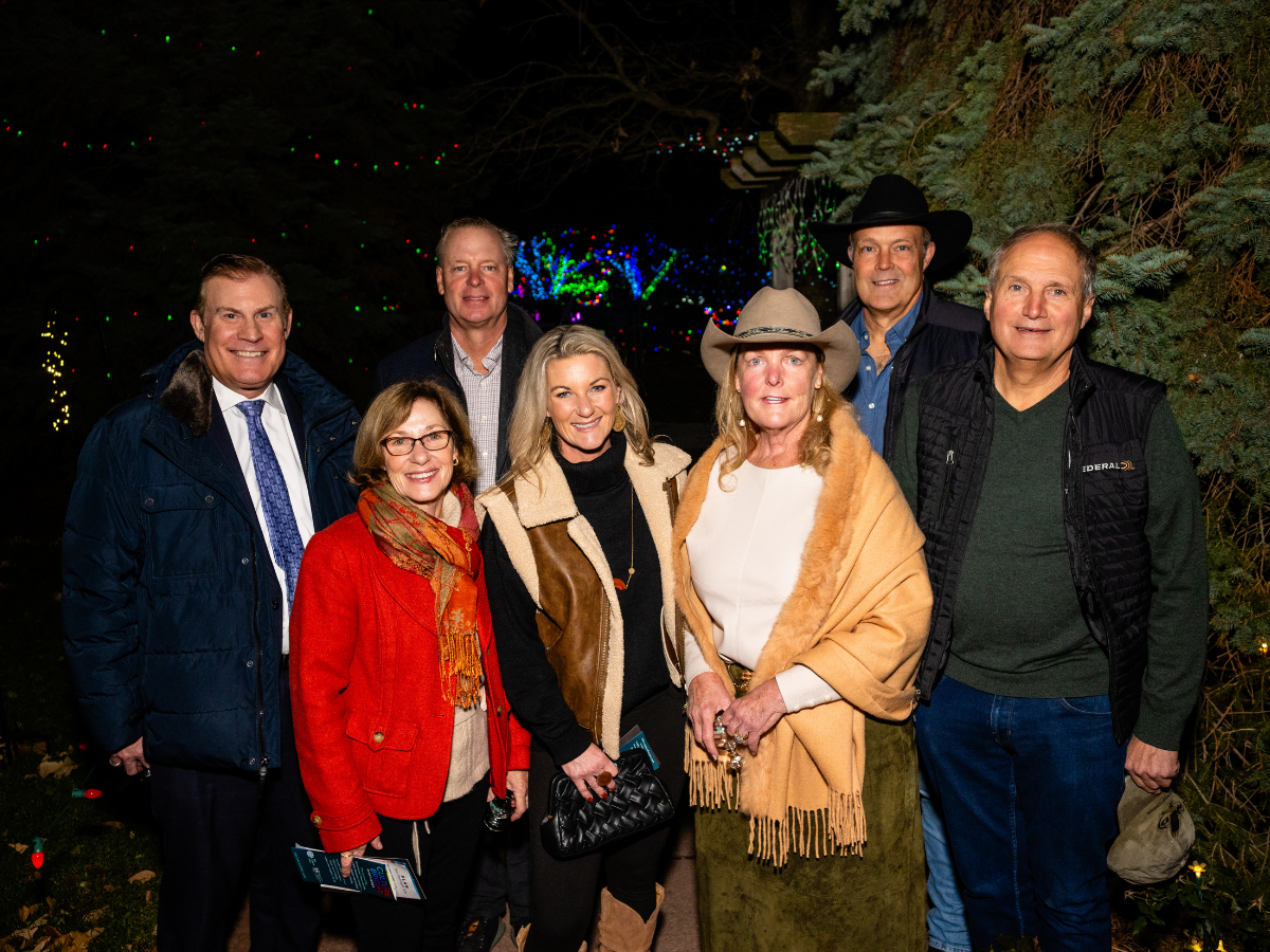 Seven people standing outdoors at night with holiday lights in the background.