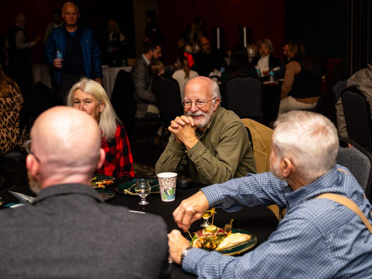 Group of seniors enjoying a social dinner at a banquet or party, sitting around a table with food and drinks, smiling and engaging in conversation.