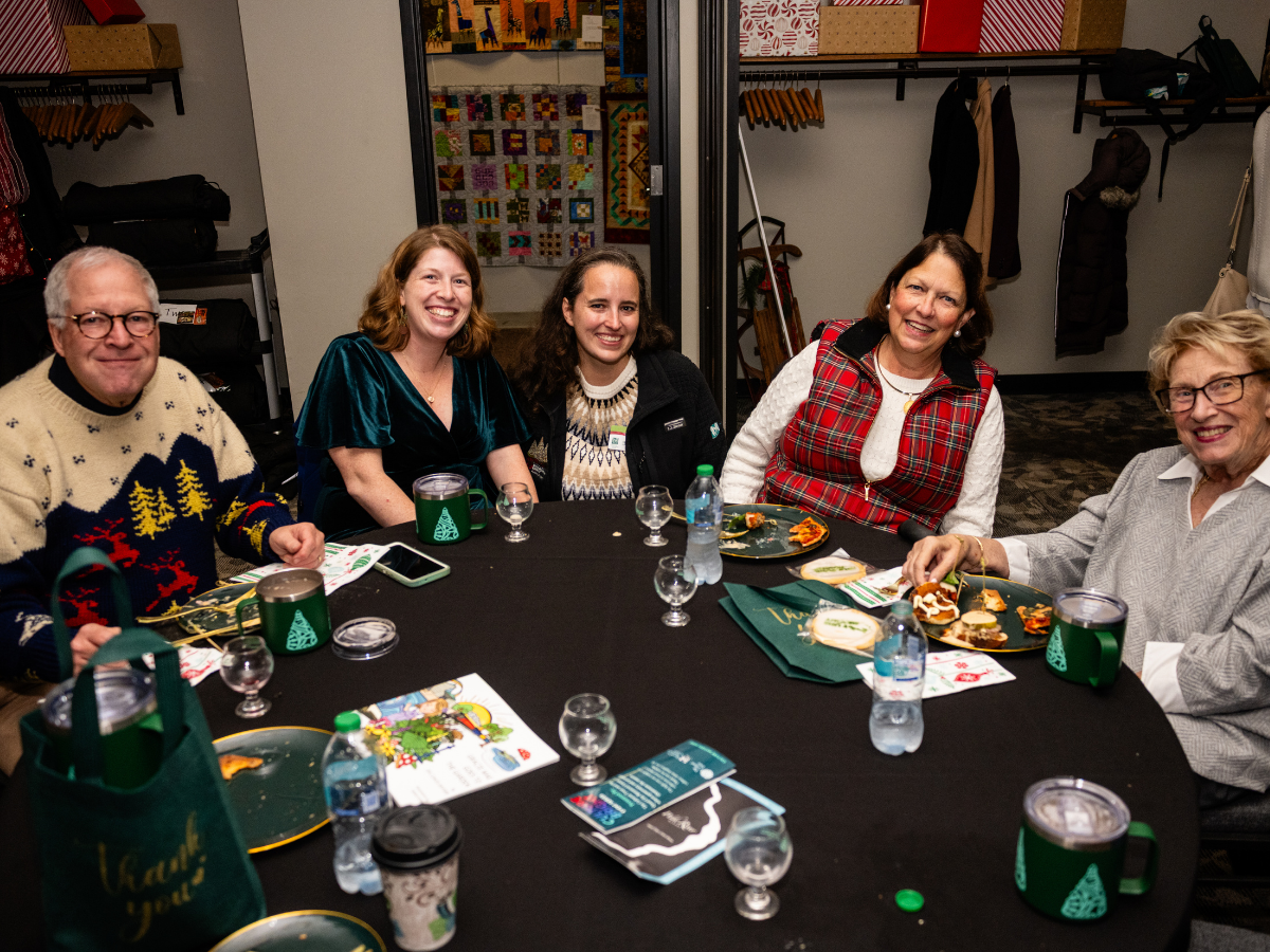 Five people sitting at a round table enjoying a holiday gathering with dessert, drinks, and holiday decorations.