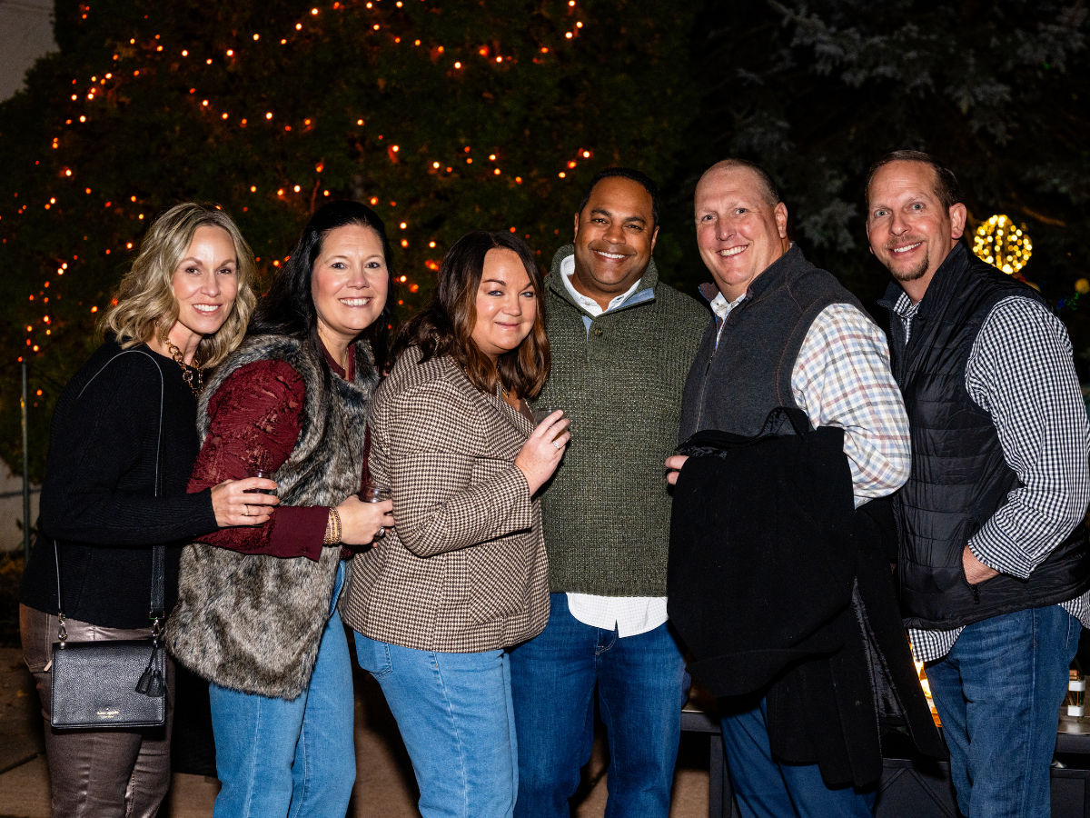 Group of seven people posing outdoors near a decorated Christmas tree at night.