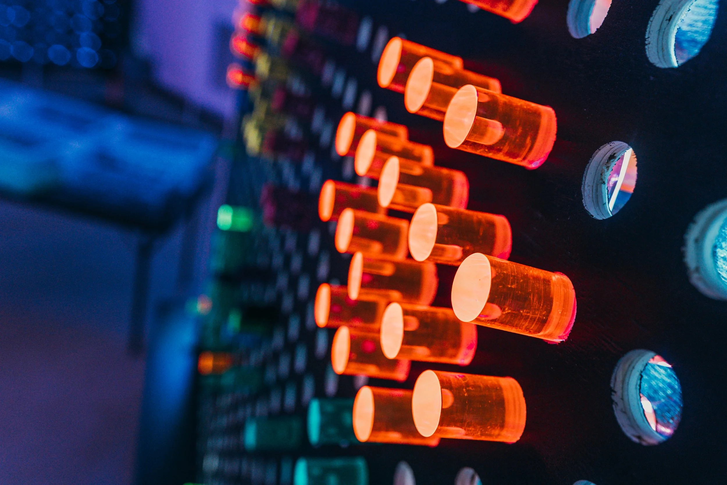 Close-up of glowing orange glass tubes arranged in a row on a dark electronic panel with various circular ports and colorful illuminated components.