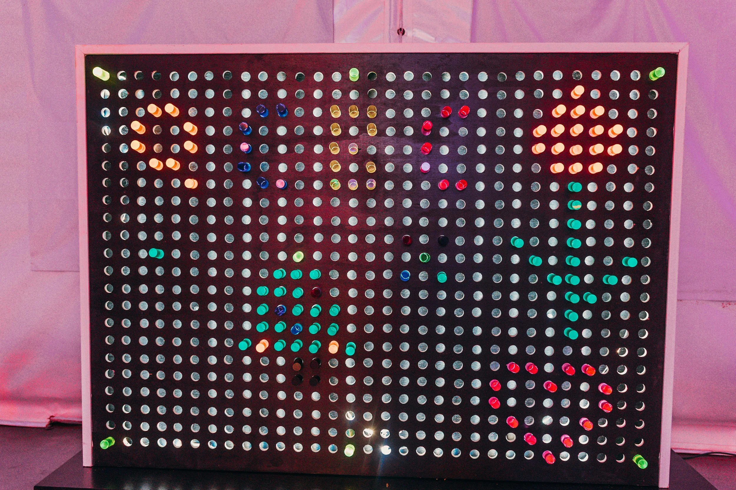 A colorful light display on a black grid with small circular lights arranged in a pattern, framed by a white border, and placed on a black surface.