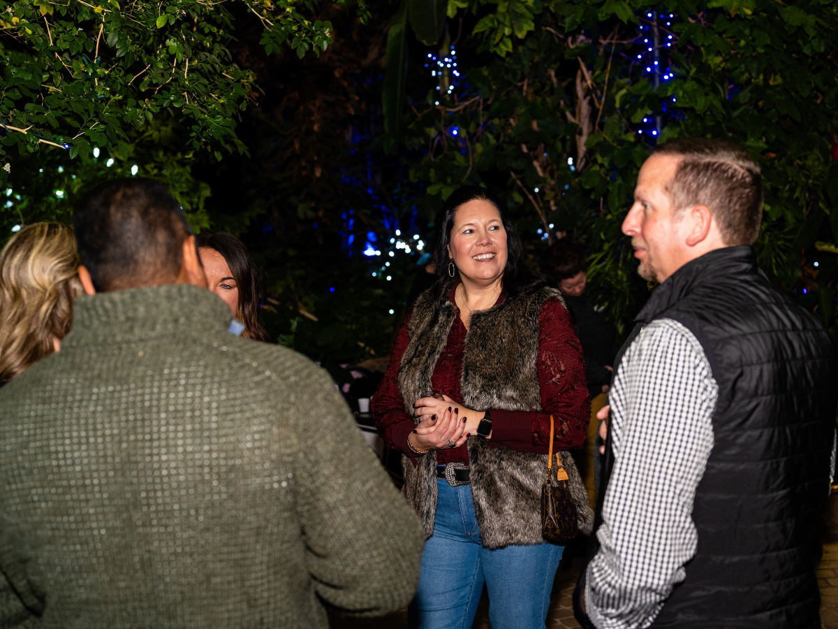 Group of five people talking in outdoors at night, with trees and string lights in the background.