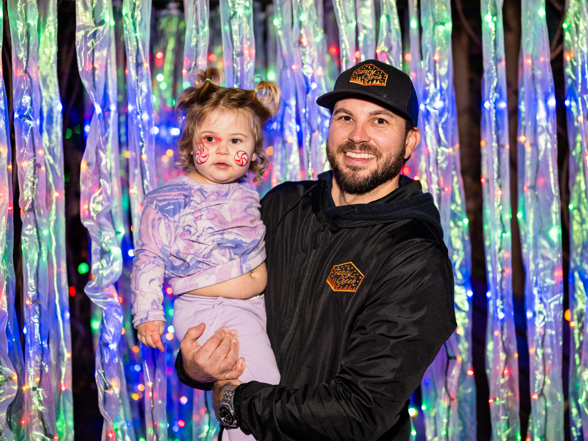 A man holding a young girl in front of a colorful, light-up Christmas decoration background.