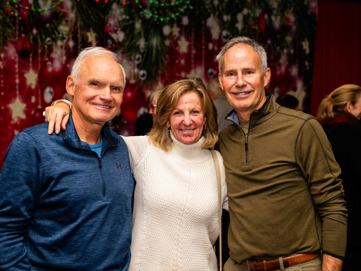 Three smiling adults posing together at a festive event with Christmas decorations in the background.