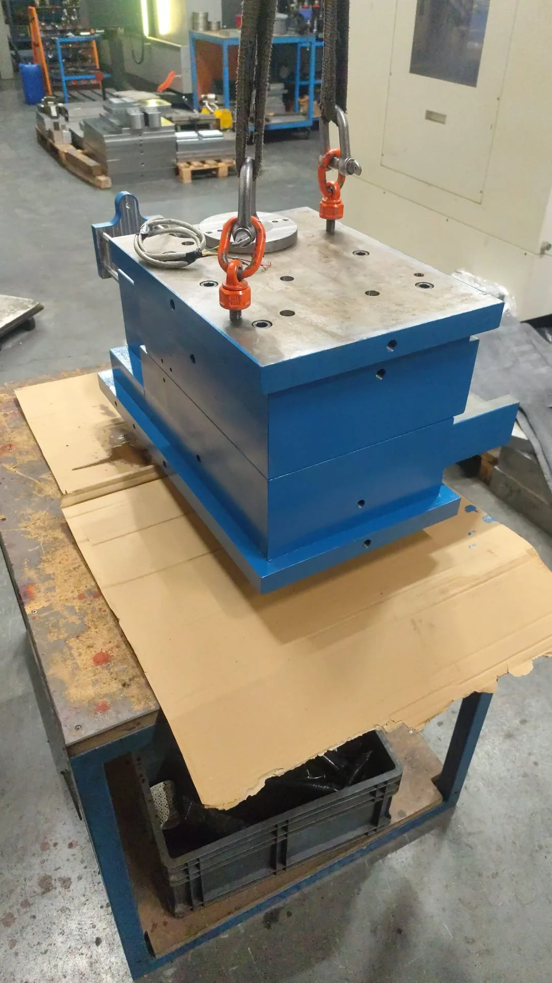 Blue metal mold placed on a wooden board on a worktable in an industrial workshop.