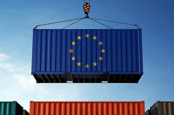A large blue shipping container with the European Union flag painted on it, featuring a circle of yellow stars. It is being lifted by a crane against a clear blue sky.