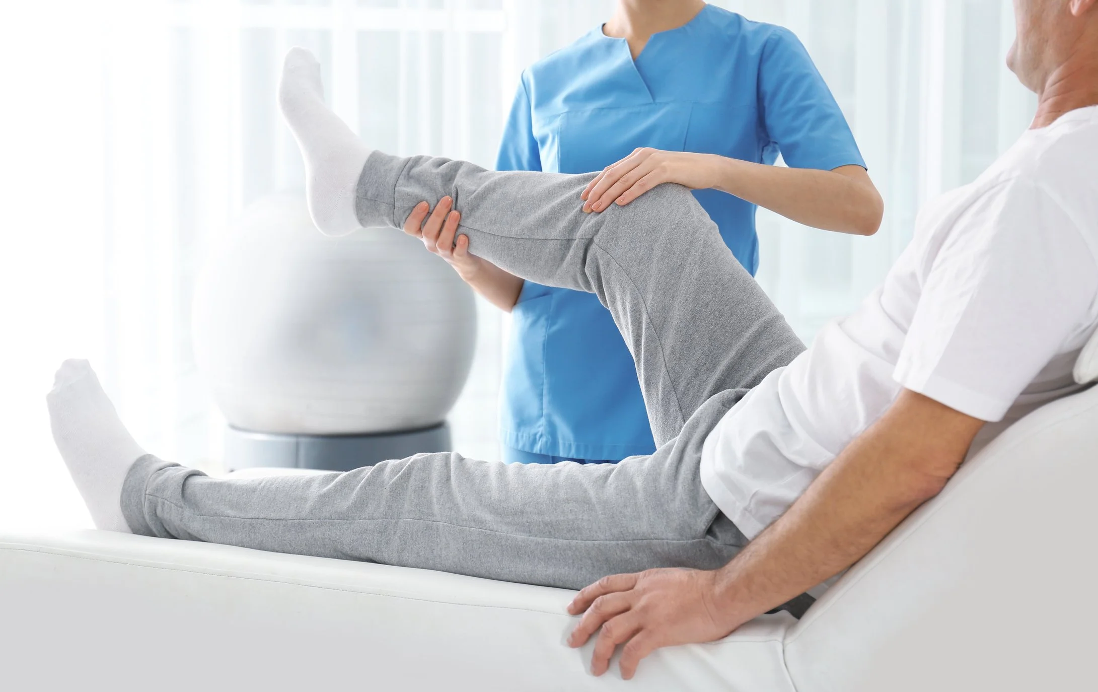 Medical professional assisting a patient with leg exercises in a clinical setting